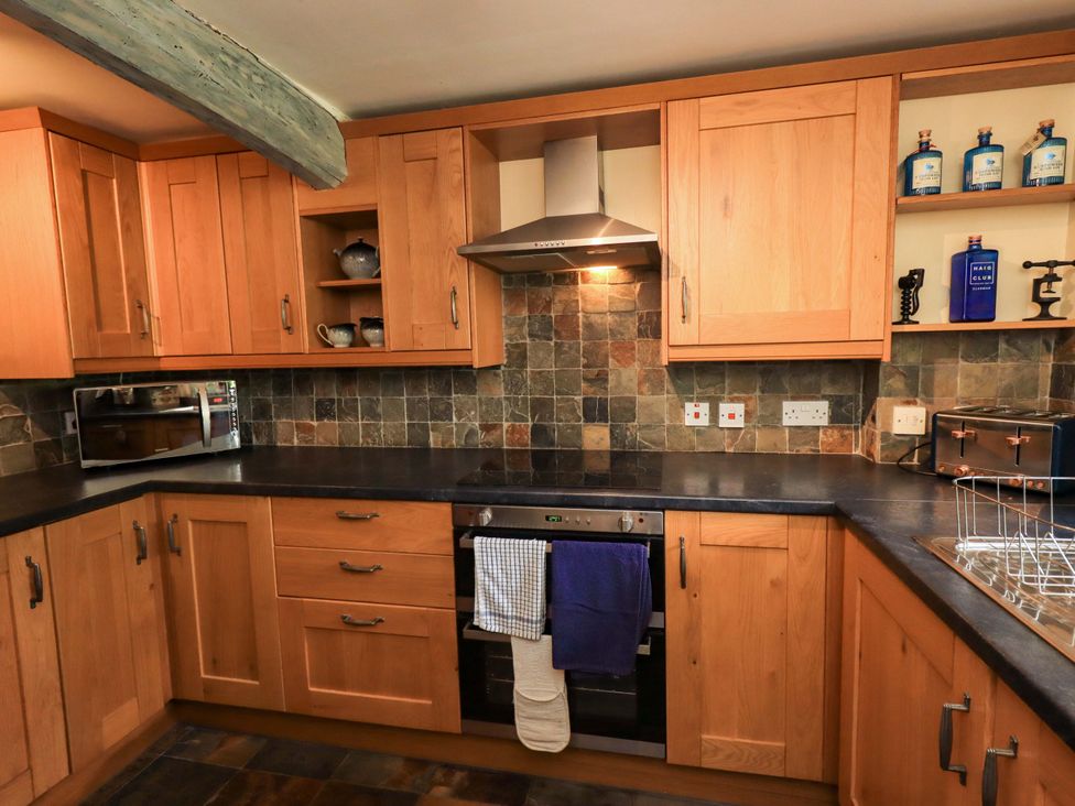 A kitchen with wooden cabinets and appliances at Tethera Cottage in Bampton, Cumbria