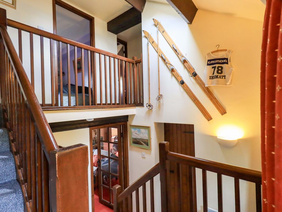 A hallway with a staircase and skis on the wall at Tethera Cottage in Bampton, Cumbria
