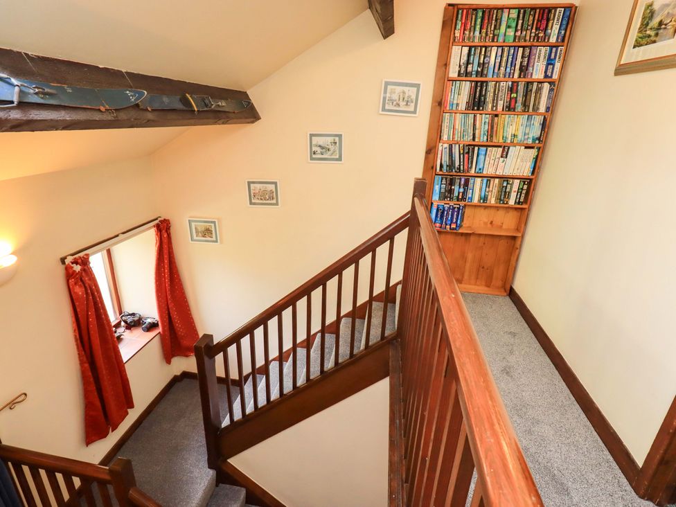 A staircase with a bookshelf and window at Tethera Cottage Bampton, Cumbria