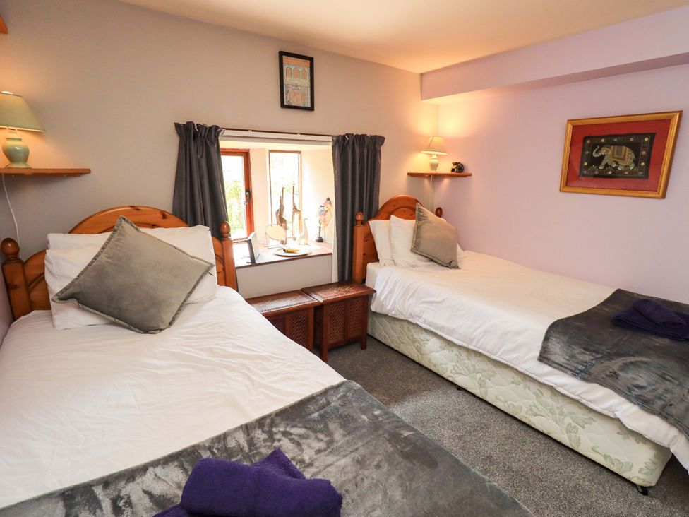 A bedroom with two beds and a window at Tethera Cottage in Bampton, Cumbria