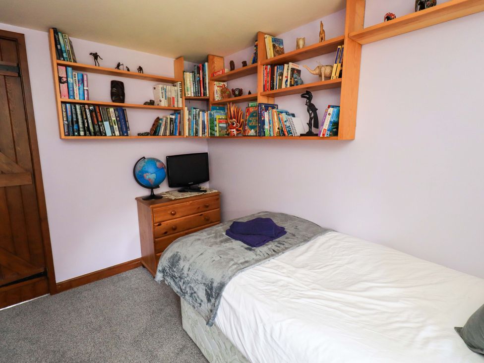 A bedroom with a bed and bookshelves at Tethera Cottage in Bampton, Cumbria
