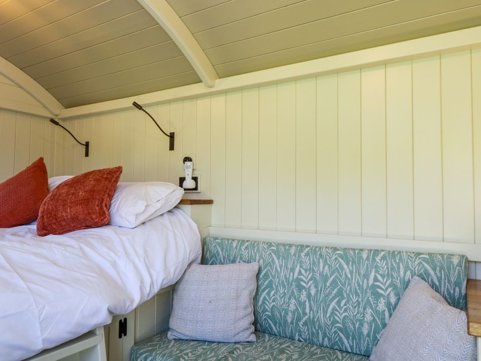 A bedroom corner with a bed having white sheets and red pillows next to a green floral patterned bench with gray cushions at Hazel South Leigh near Witney