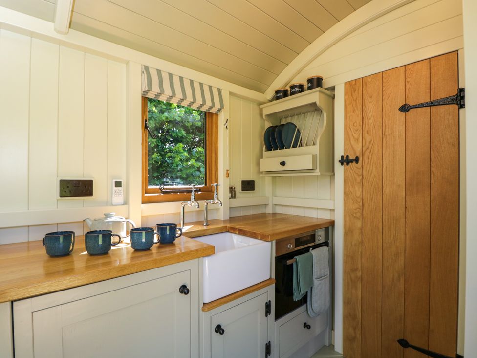 A small kitchen with wooden countertops blue mugs on the counter a white sink and a wooden door at Hazel South Leigh near Witney