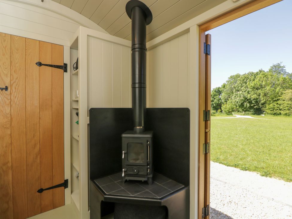 A corner wood burning stove next to a wooden door with iron hinges and an open door showing a grassy outdoor area at Hazel South Leigh near Witney