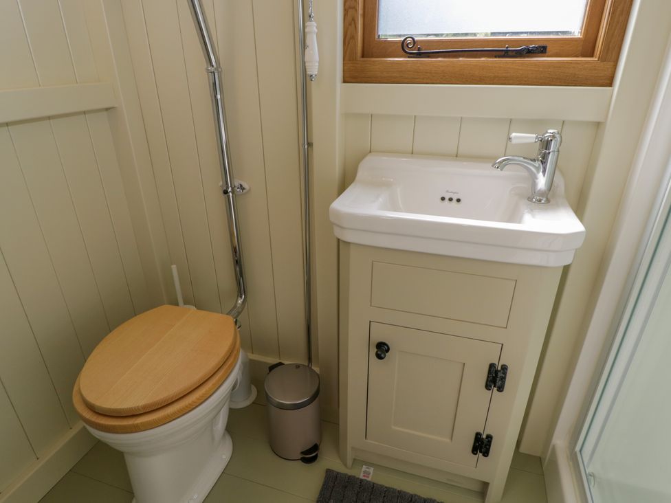A small bathroom with a toilet with a wooden seat a white sink with a cabinet and a window above at Hazel in South Leigh near Witney