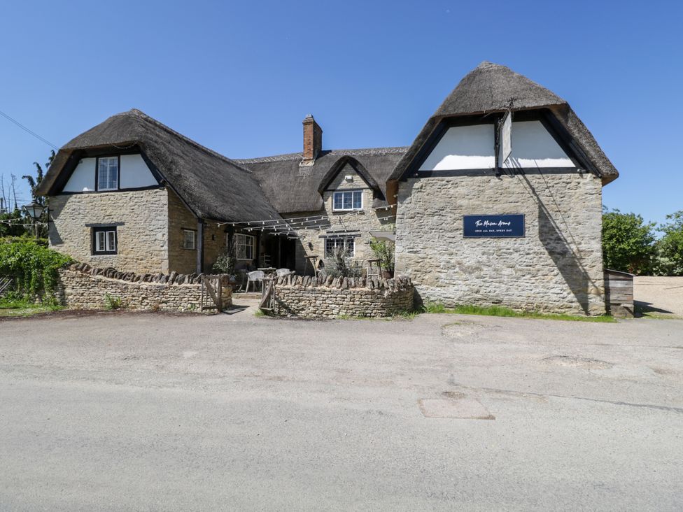 A stone building with a thatched roof and outdoor seating area by a road at Hazel South Leigh near Witney