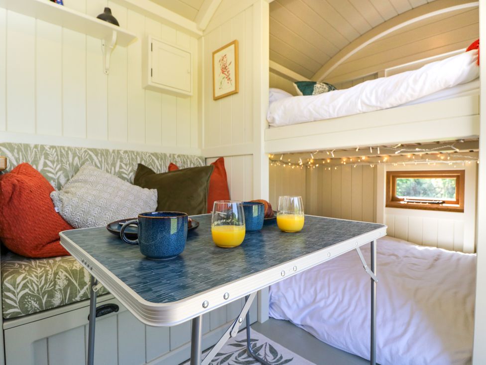 A small interior space with a table holding mugs and glasses of orange juice near cushioned bench seating and a bunk bed with string lights at Spindle in South Leigh near Witney