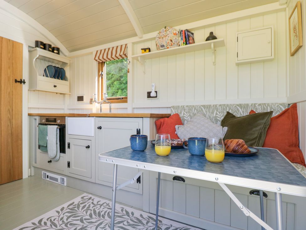 A kitchen area with a table set with drinks and pastries next to a cushioned bench with pillows at Spindle South Leigh near Witney