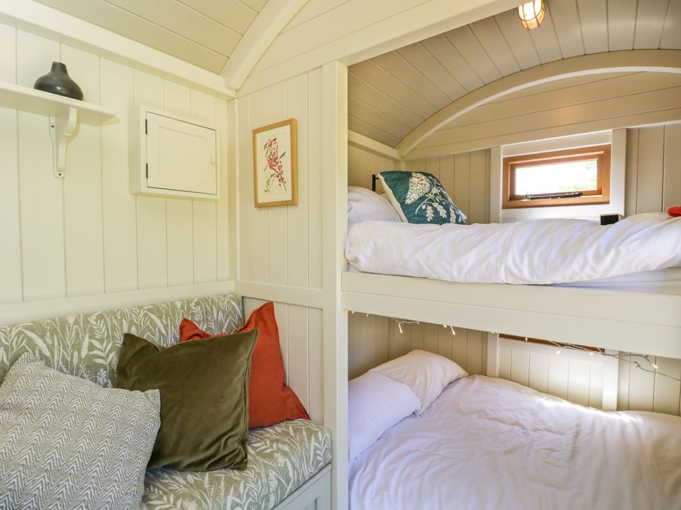 A small bedroom with bunk beds and a cushioned bench seat with pillows at Spindle South Leigh near Witney