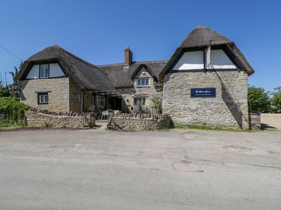 A stone building with thatched roof and outdoor seating behind a low stone wall at Spindle South Leigh near Witney