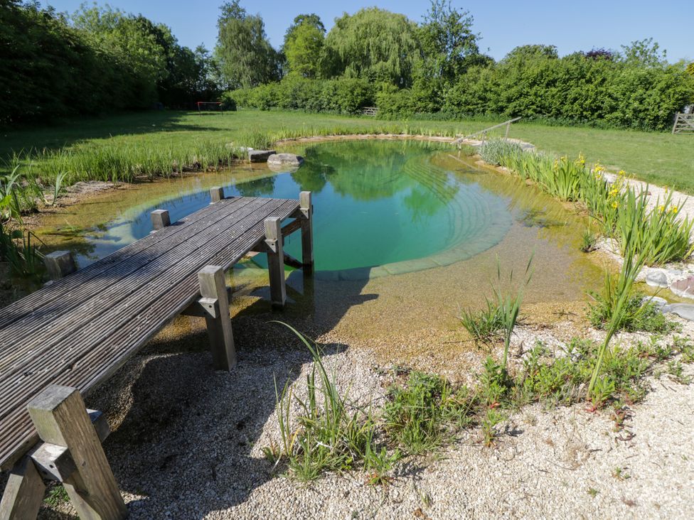 A natural swimming pond with a wooden jetty and surrounding plants in a grassy area at Spindle South Leigh near Witney