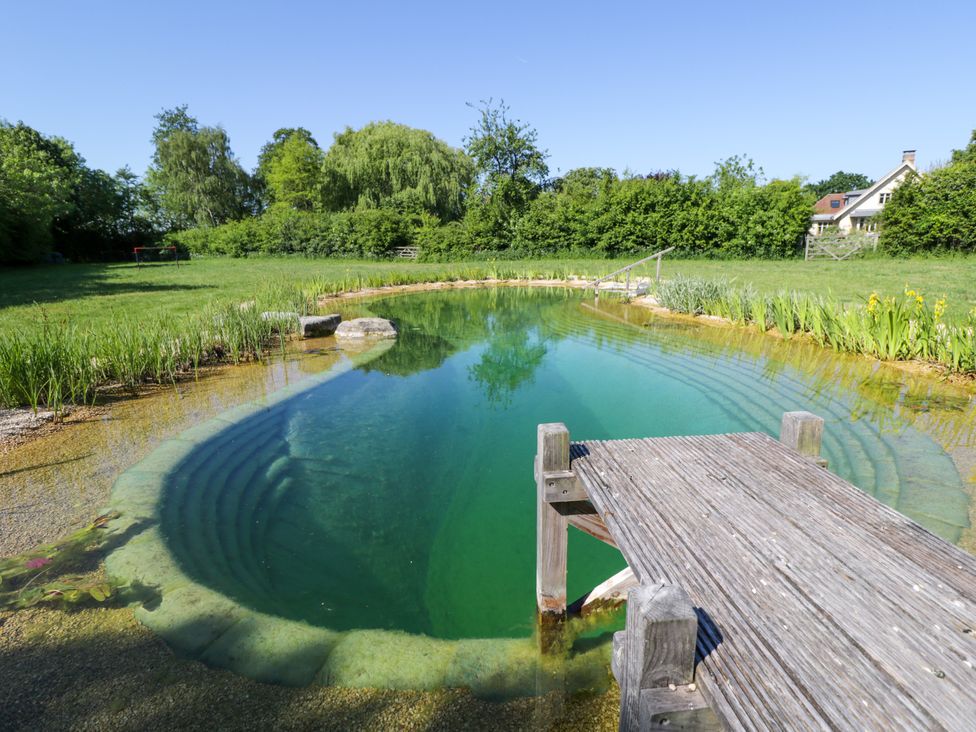 A natural swimming pond with wooden deck and surrounding grass and trees at Spindle in South Leigh near Witney