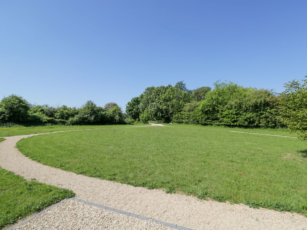 A curved gravel path around a grass field with trees and bushes at Spindle in South Leigh near Witney