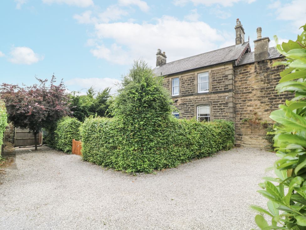 An outdoor view of a house surrounded by greenery and a gravel driveway at Deeley House in Darley Dale