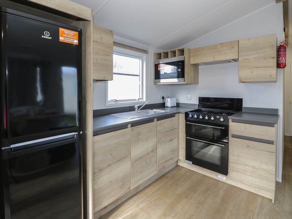 A kitchen with appliances and wooden storage at Lido Silver Plus 111 Prestatyn