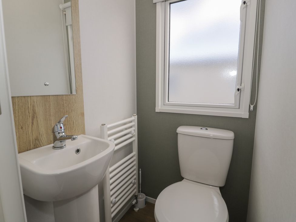 A bathroom with a toilet, sink, mirror, and radiator at Lido Silver Plus 111 Prestatyn
