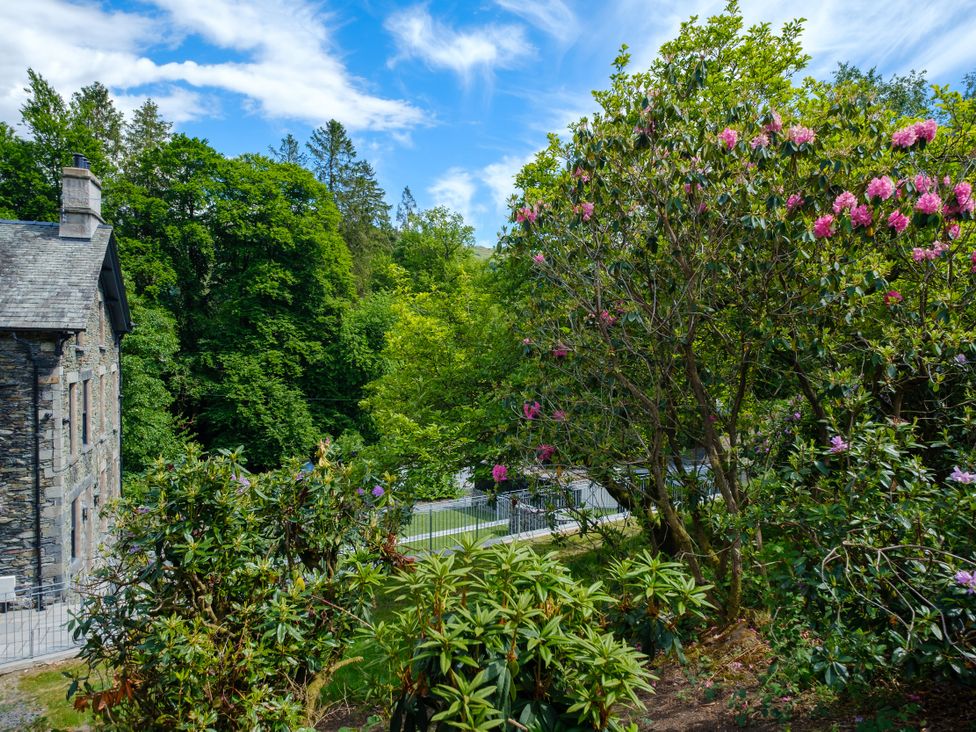 An outdoor area with a building beside trees and flowers at Riverside in Ambleside