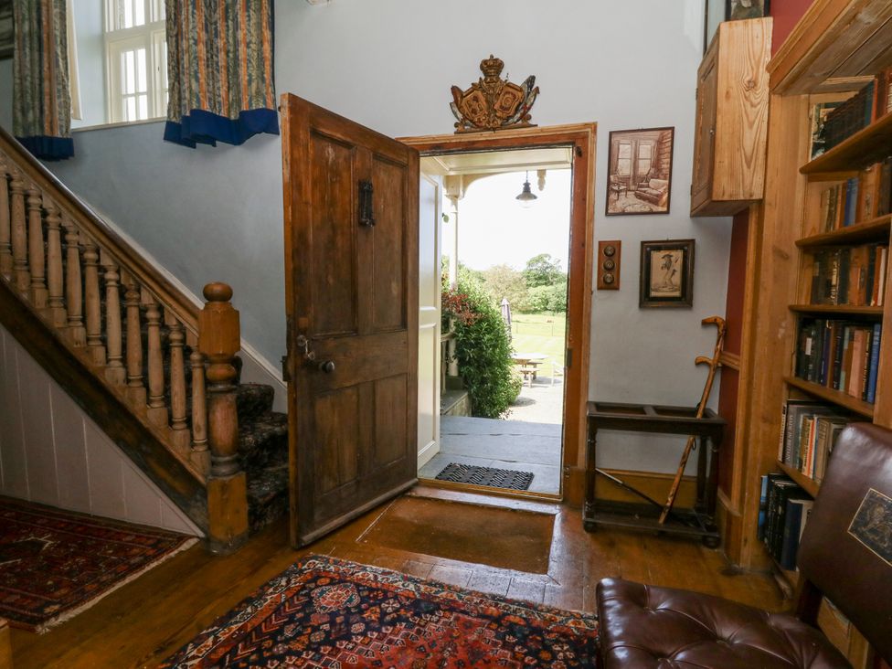 A hallway with a staircase, front door, and bookshelf at Plas Pontfaen near Fishguard and Newport, Pembrokeshire