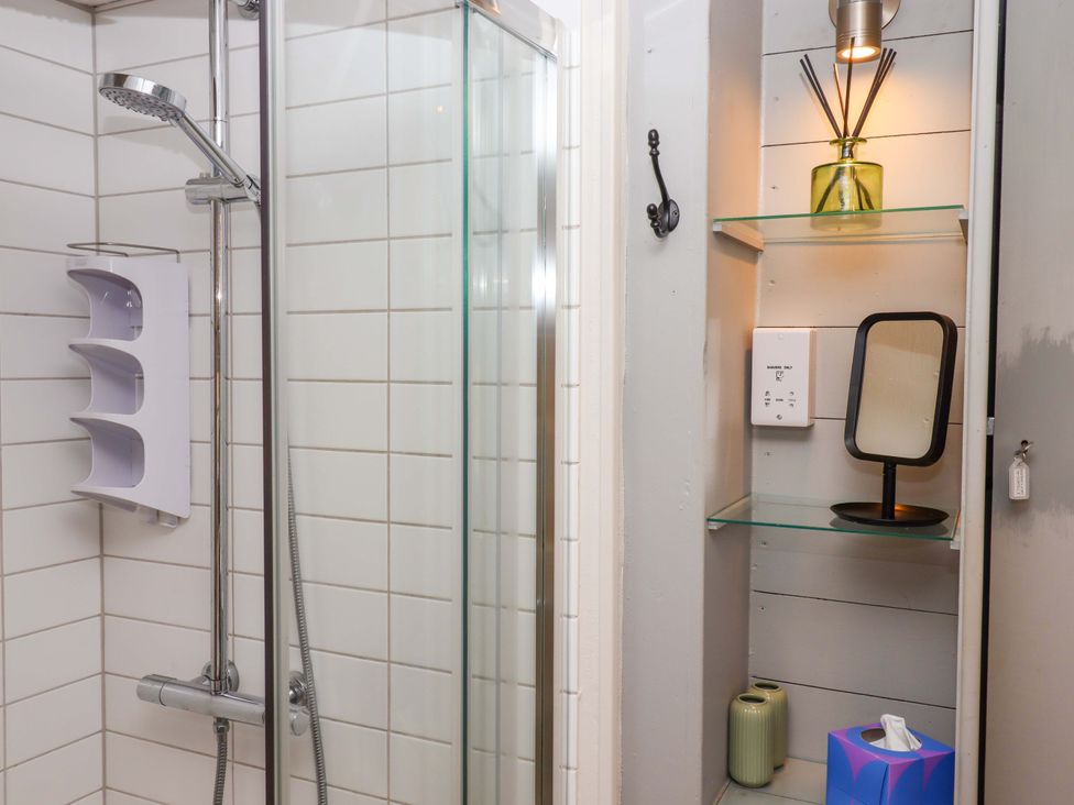 A bathroom with a shower and shelves containing a mirror and decorative items at 1 Myrtle Cottages Stokeinteignhead