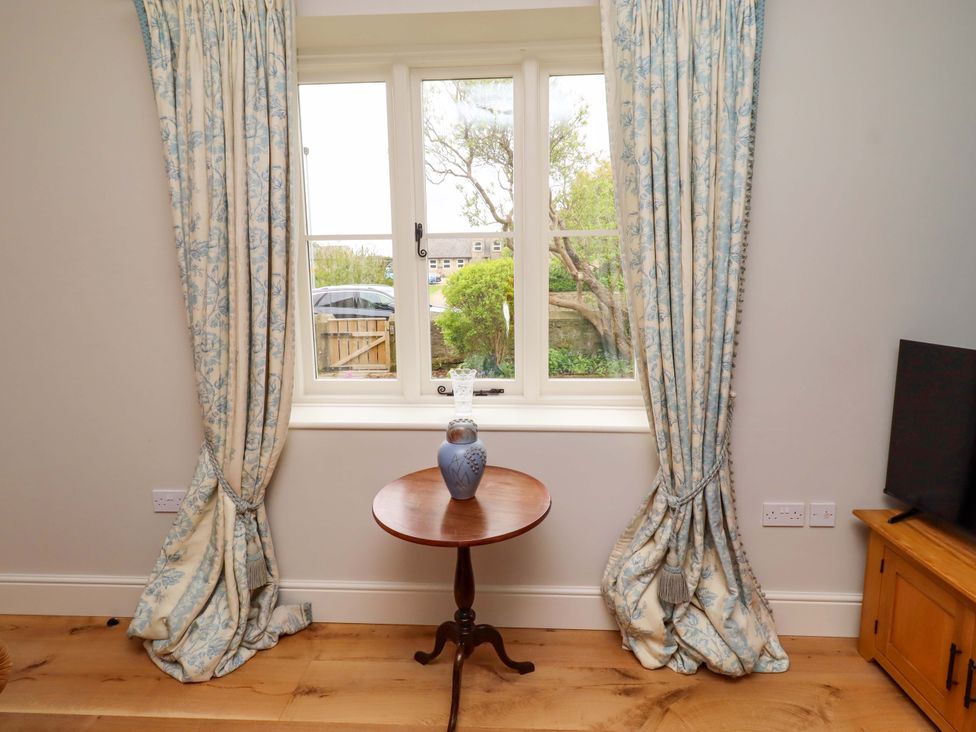 A living room with a table and vase by a window at 9 Longhirst Village in Morpeth