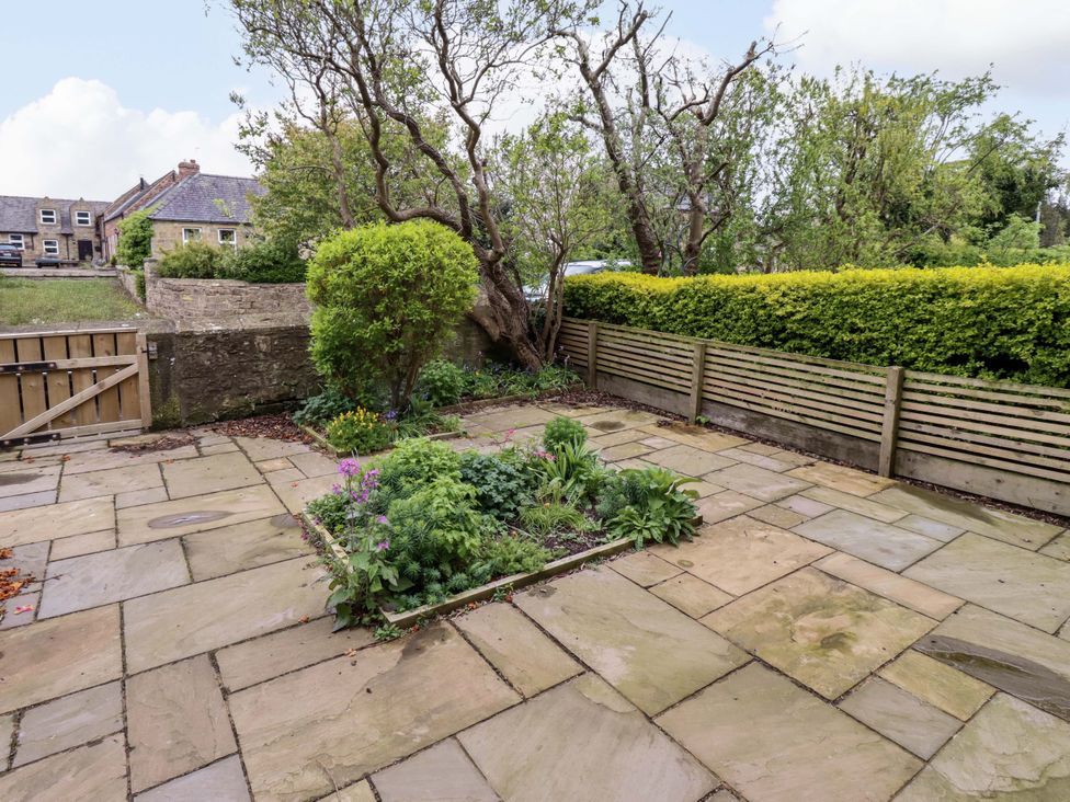 A garden area with a patio and flowerbed at 9 Longhirst Village in Morpeth