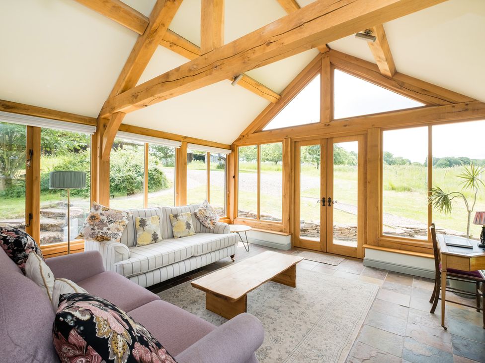 A conservatory with a sofa, table, and glass doors at Henhouse Farm in Bodenham