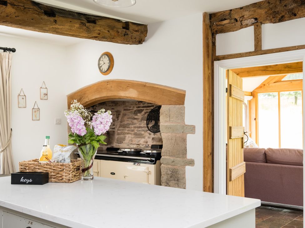 A kitchen with flowers on a counter and an open doorway to a living area at Henhouse Farm Bodenham