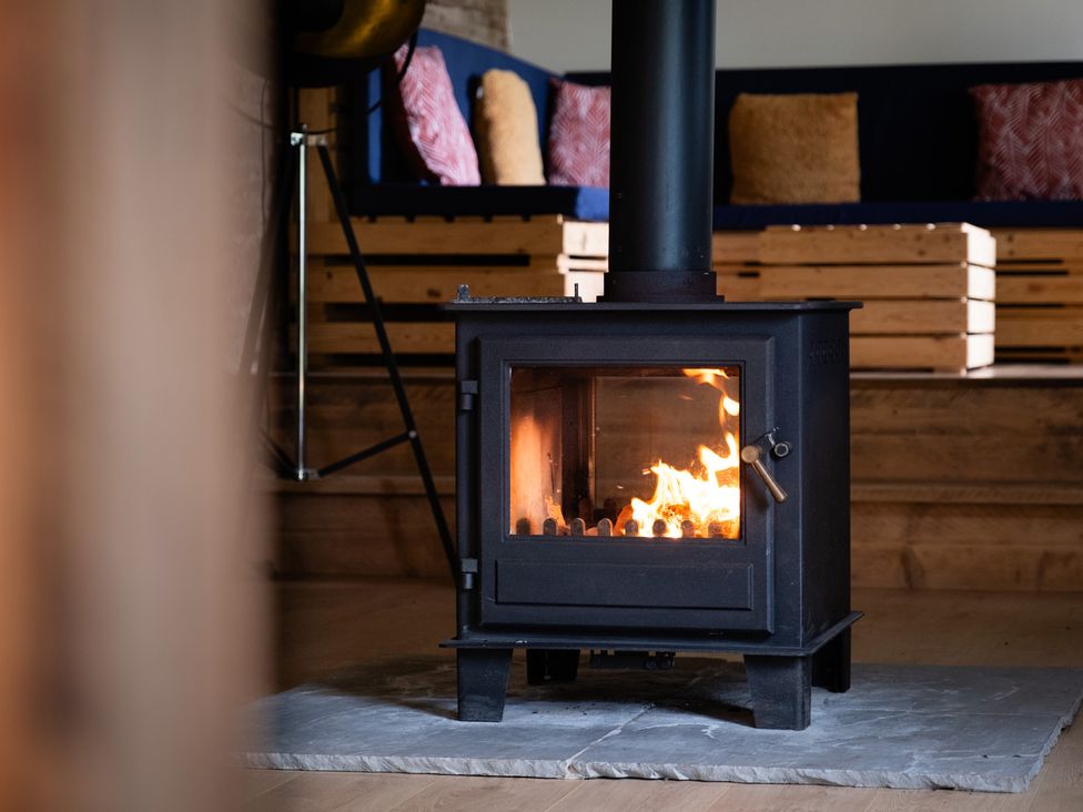 A wood stove with flame in a living room at Henhouse Farm in Bodenham