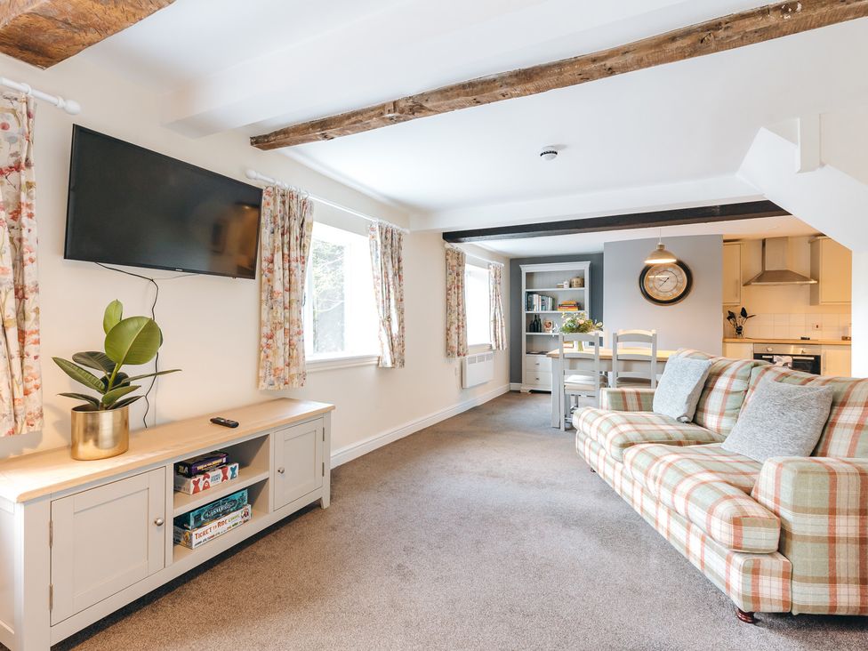A living room with a wall-mounted television a cabinet with board games a plaid sofa and a dining table with chairs at The Pheasant Apartment in Neenton