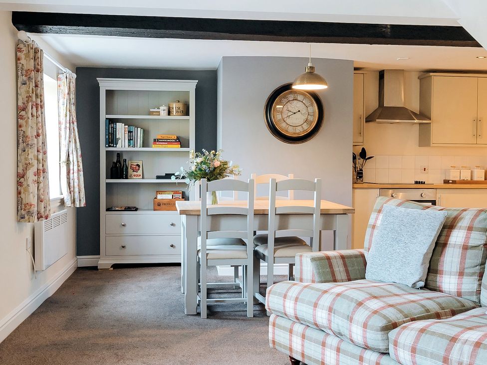A dining area with a table and chairs next to a kitchen and a plaid sofa in a living room at The Pheasant Apartment in Neenton