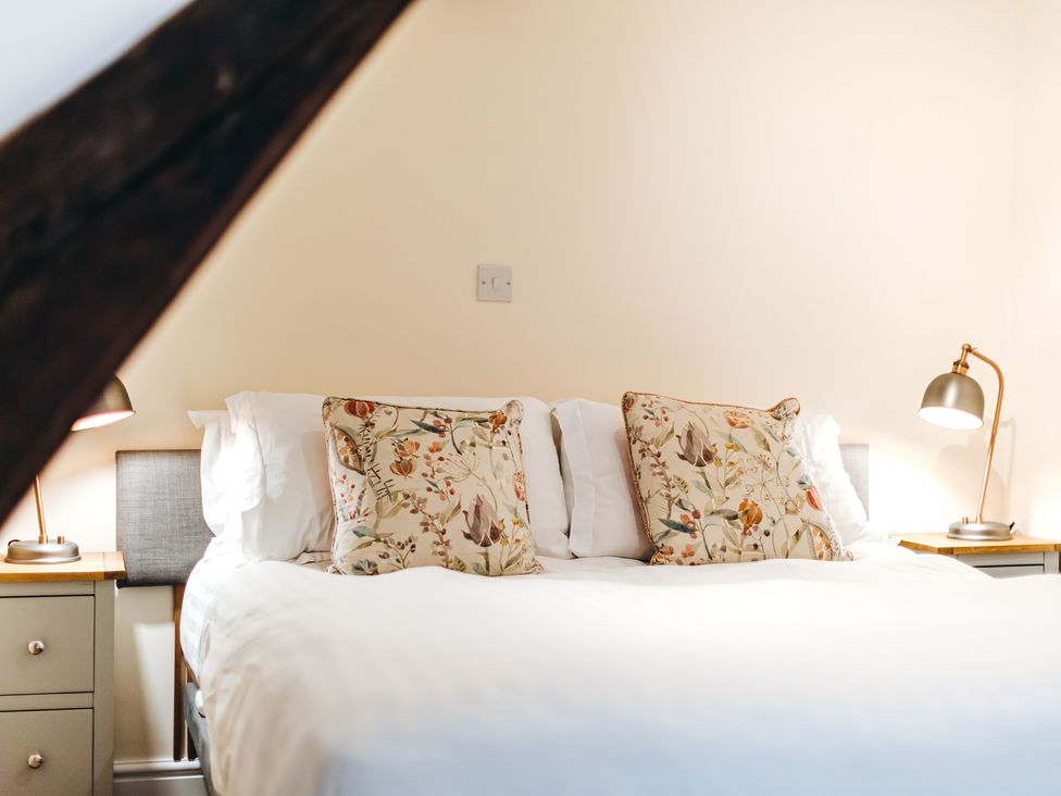 A bedroom with a bed with floral cushions and two bedside tables with lamps at The Pheasant Apartment in Neenton