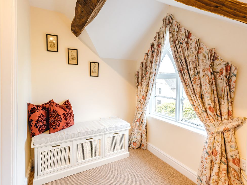A small seating area with a white cushioned bench red pillows floral curtains and framed pictures on the wall at The Pheasant Apartment in Neenton