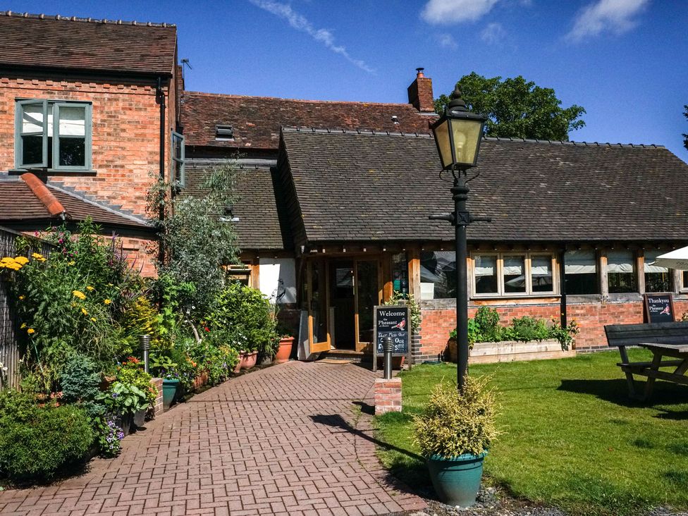 A brick building with a garden pathway surrounded by plants and a lamp post in front at The Pheasant Apartment in Neenton