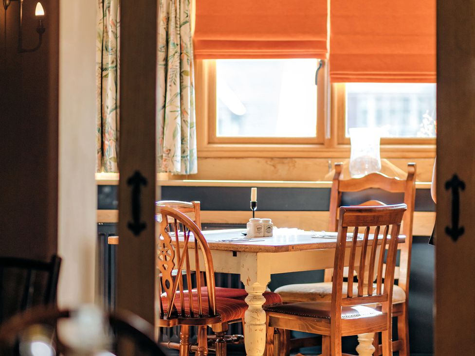 A dining table with four wooden chairs near windows with orange blinds and floral curtains at The Pheasant Apartment in Neenton