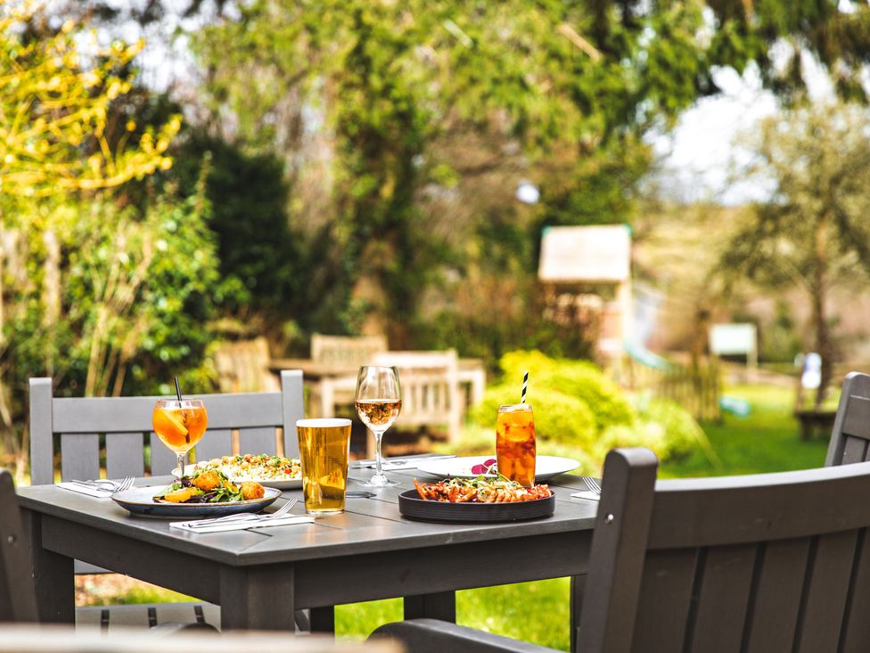 A dining table outside with plates of food and drinks surrounded by grey chairs in a garden at The Pheasant Apartment in Neenton