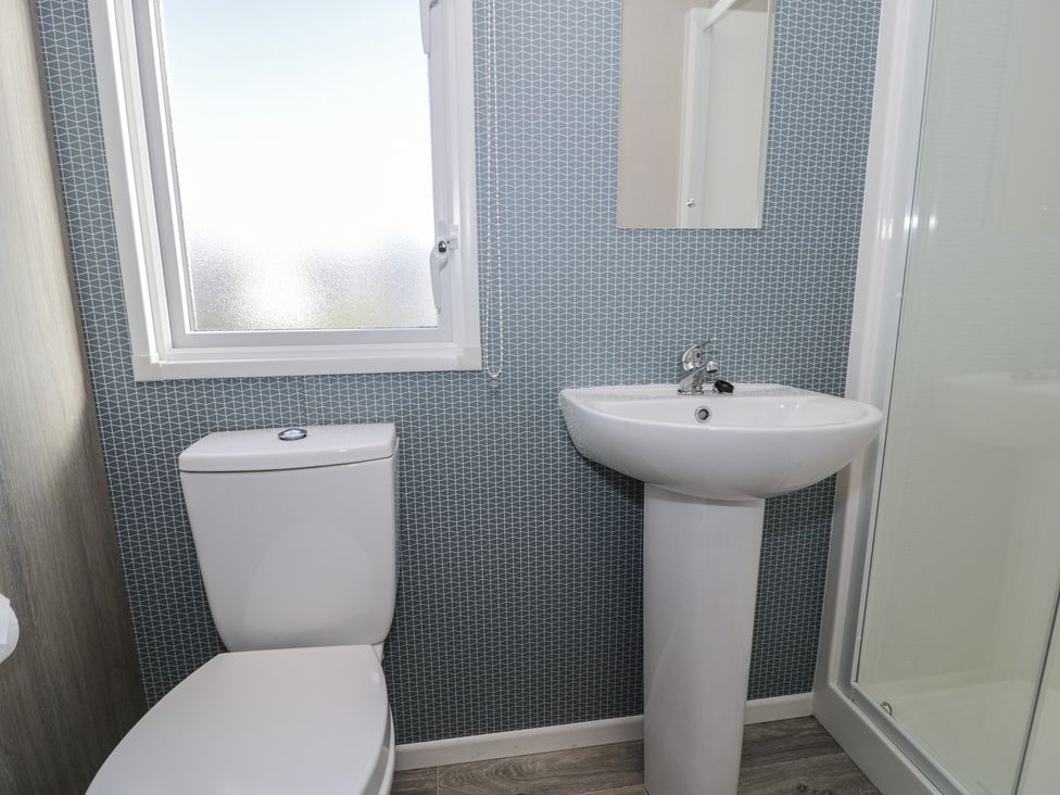 A bathroom featuring a toilet, sink, mirror and shower at Lido Gold 120 in Prestatyn