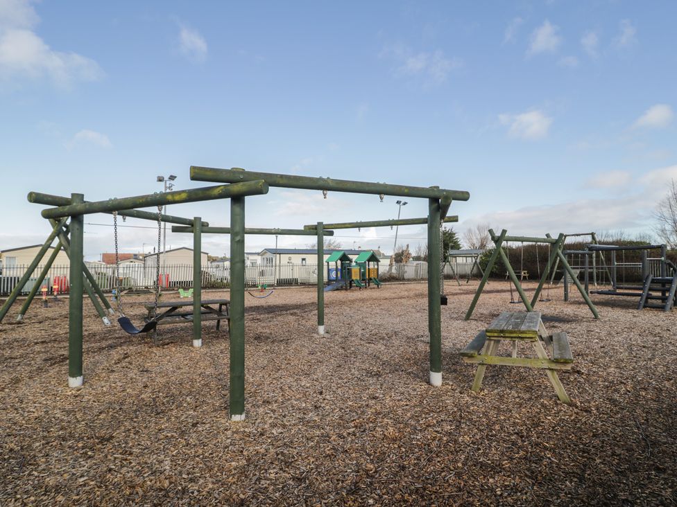 A playground with swings and picnic table at Lido Gold 120 Prestatyn