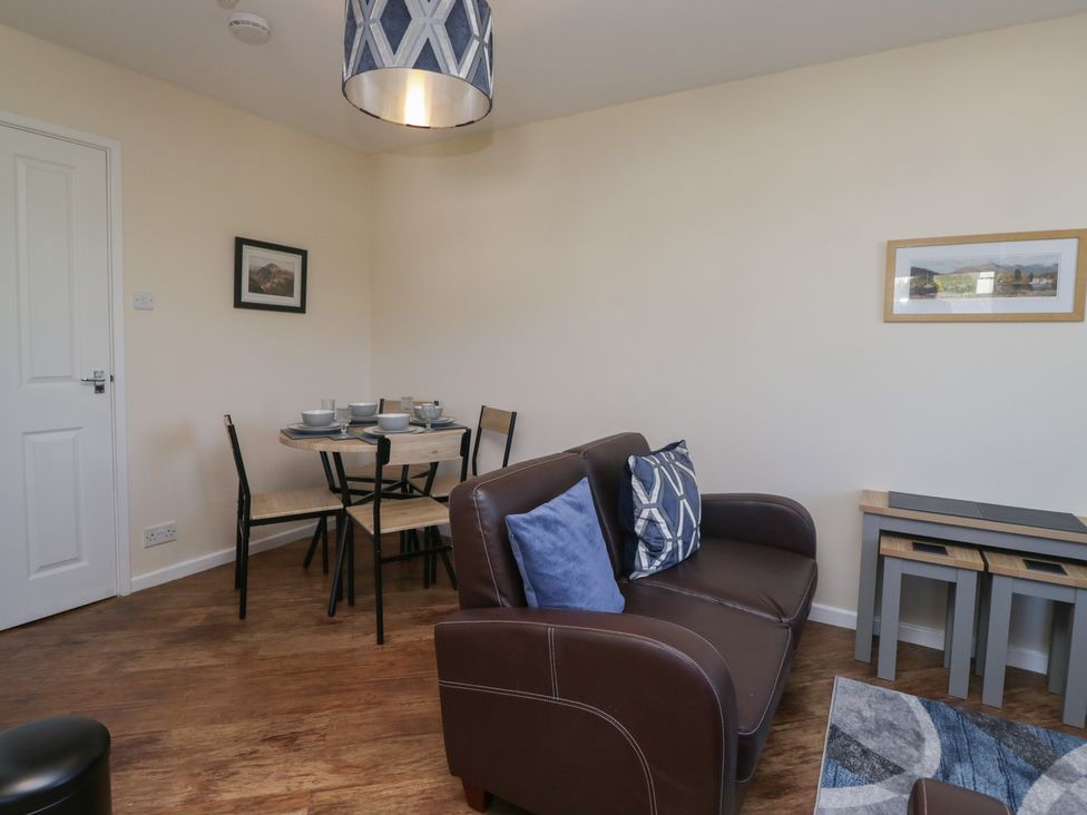 A small dining area with a round table and four chairs and a brown sofa with pillows in a living room at Eves Attic in Bowness On Windermere