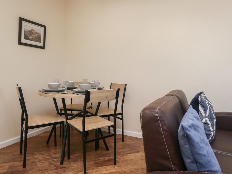 A dining area with a round wooden table set with bowls and glasses four wooden chairs and a brown leather sofa with blue cushions at Eves Attic in Bowness-On-Windermere