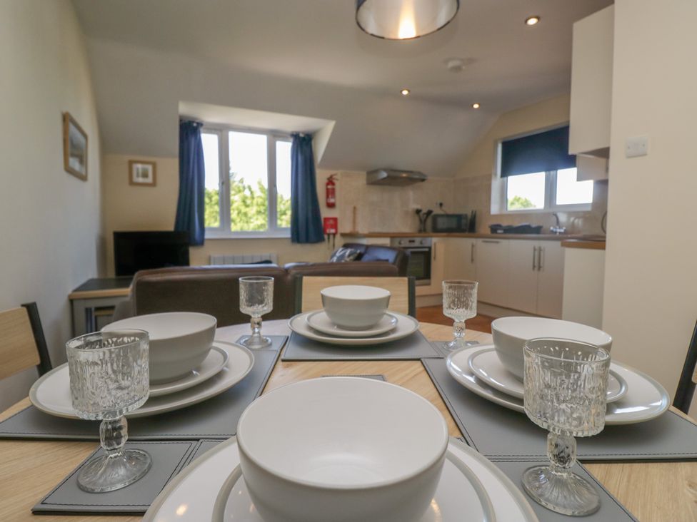 A dining table set with white bowls plates and glasses in a room with a kitchen and living area at Eve's Attic in Bowness-On-Windermere