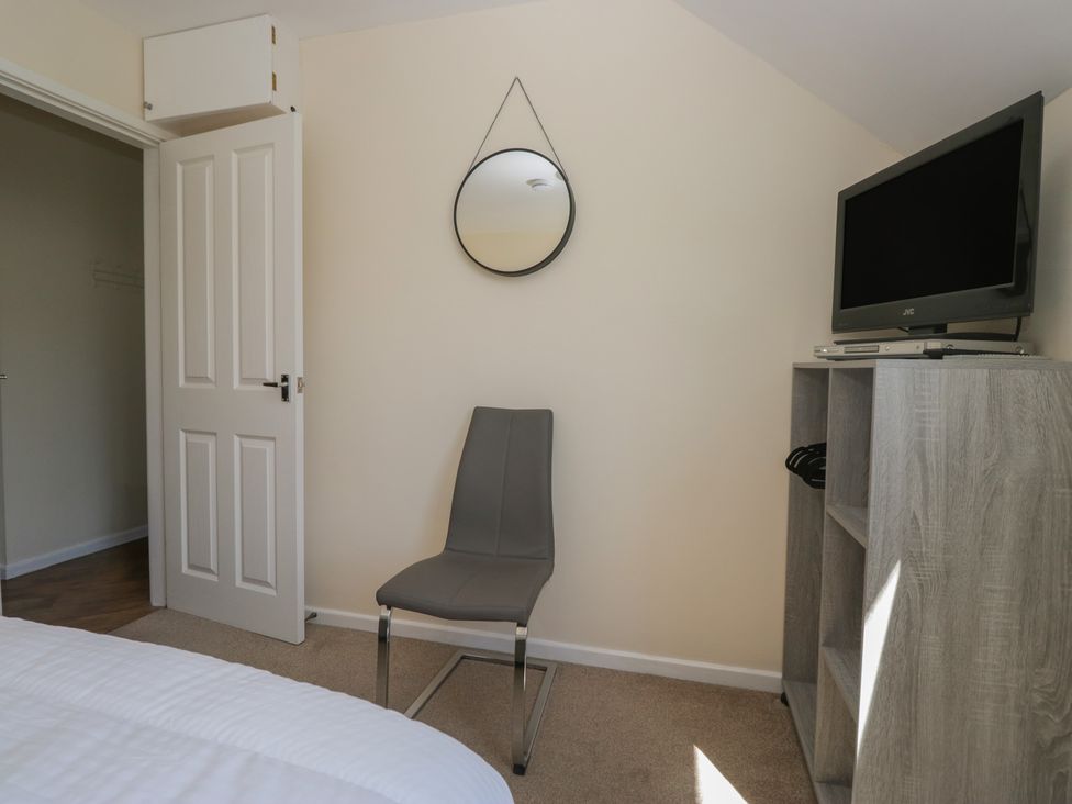 A bedroom with a gray chair under a round mirror and a wooden cabinet with a television at Eves Attic in Bowness-On-Windermere