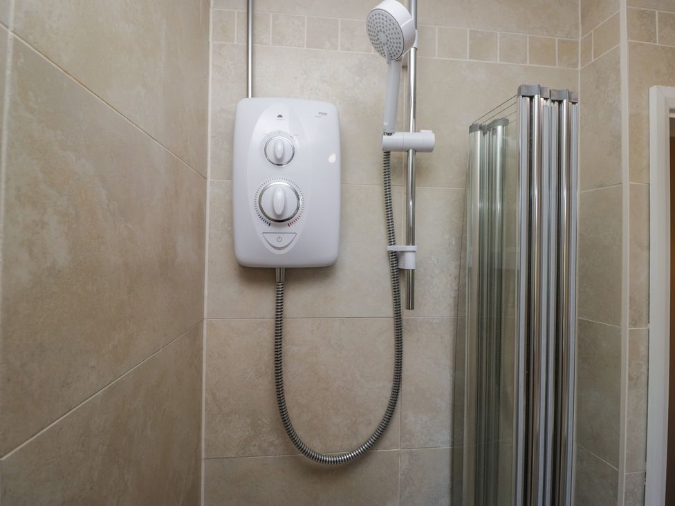 A shower unit with adjustable shower head and controls in a tiled shower enclosure at Eves Attic in Bowness-On-Windermere