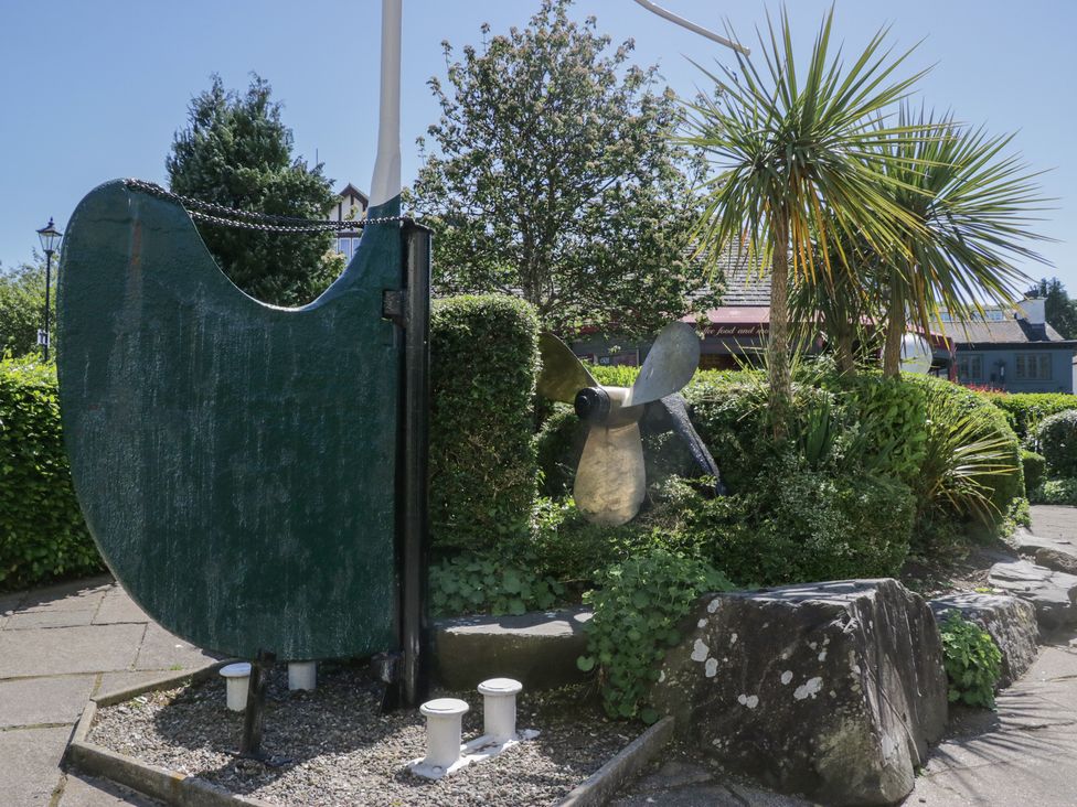 An outdoor scene with a large green ship rudder and a metal propeller surrounded by greenery and rocks at Eves Attic in Bowness-On-Windermere