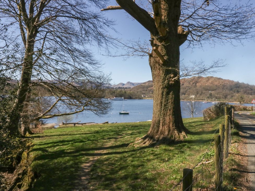 A lakeside scene with trees a path and boats on the water near hills at Eves Attic in Bowness-On-Windermere