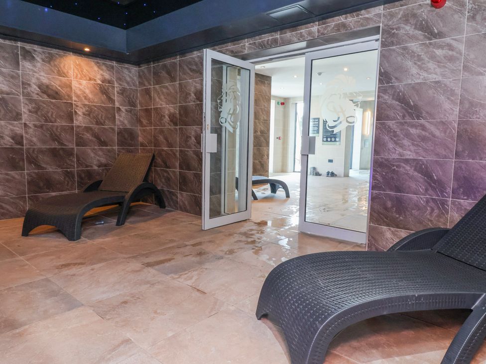 An indoor pool area with chaise lounges and a glass door at Woodlands Platinum (WO29) in Ruthin