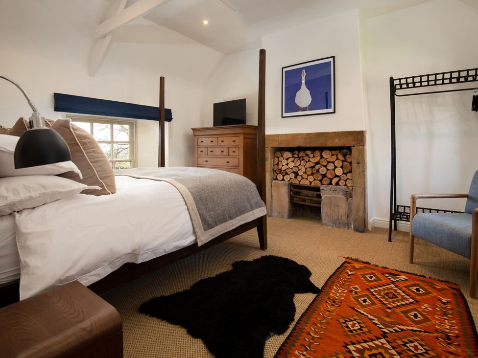 A bedroom with a bed, dresser, chair and fireplace at The Old Coach House in Eglingham near Alnwick