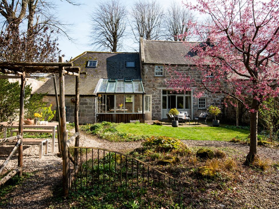 A garden with a house and a greenhouse at The Old Coach House in Eglingham near Alnwick