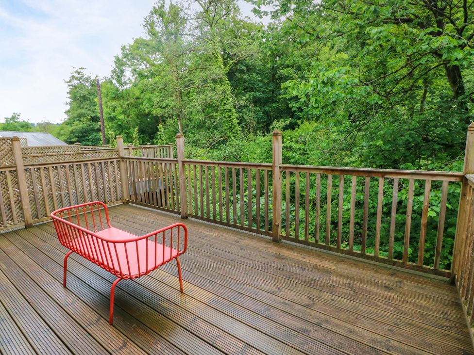 A deck area with a red chair overlooking greenery at The Old Creamery in Ffairfach