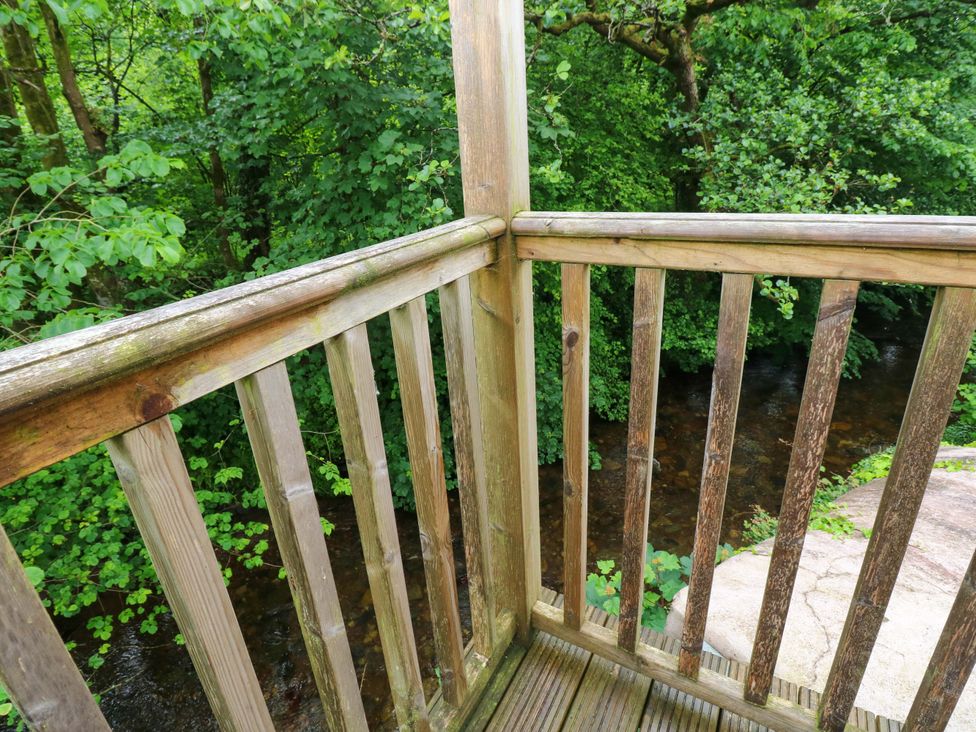 A view of a wooden deck overlooking greenery and a stream at The Old Creamery in Ffairfach