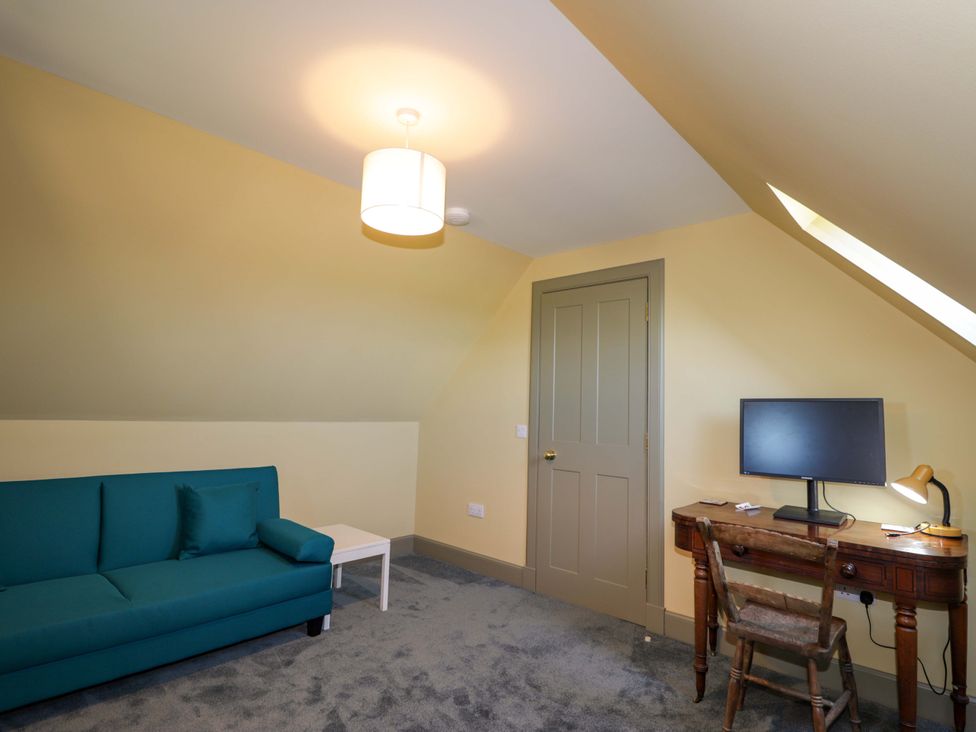 An attic room with a sofa, desk, and computer monitor at The Mandrel in Portmahomack